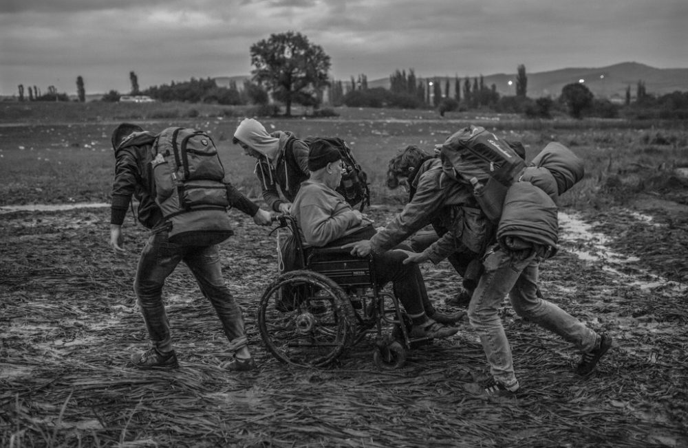 In 2015, more than one million people crossed European borders, most of them Syrian refugees escaping war and the surge of the terrorist group Islamic State in their country of origin. In this picture taken on the Balkan route, a group of Syrian friends is helping a family carrying a person in wheelchair out of mud. Most of the refugees have walked from Greece to Germany, marching towards  temporary open borders to seek asylum in Europe. During the long trajectory, they have encountered walls and obstacles, but also solidarity and support.