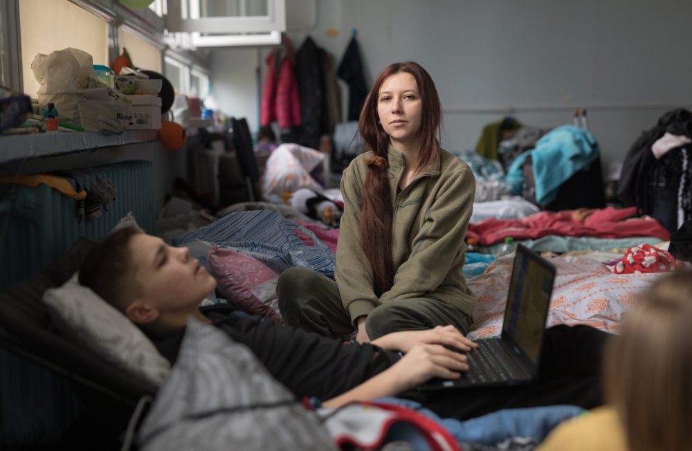 Alla is sitting on her bed in one of the classrooms. She arrived with her mother and sister from the village Menchykury, Zaporozhye region. They are staying in the shelter from the 1st of September 2022.